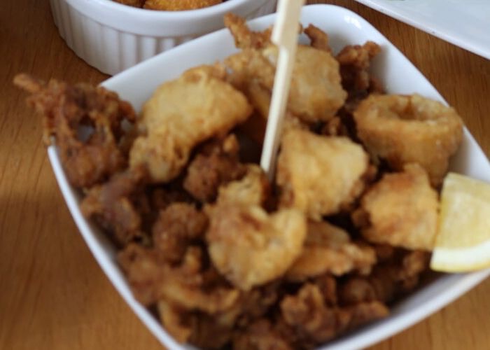 Weiße Schale mit goldbraun frittierten Calamari-Ringen und einer Zitronenspalte.